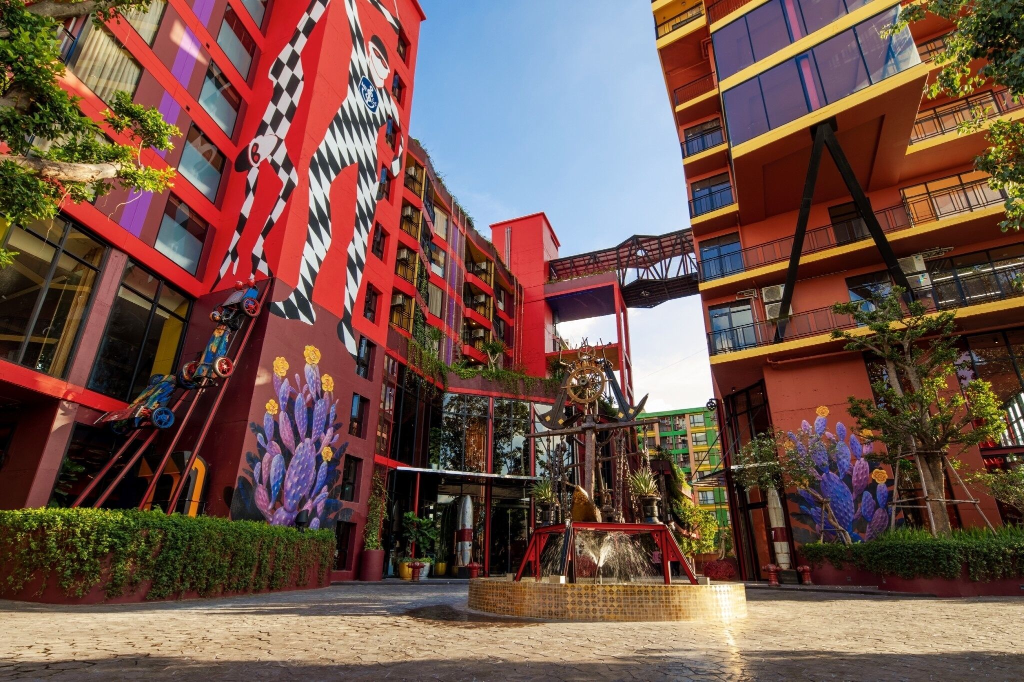 A modern building with a red and black facade, featuring a large cactus mural and a mechanical sculpture in the entrance area.