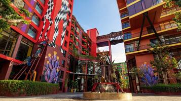 A modern building with a red and black facade, featuring a large cactus mural and a mechanical sculpture in the entrance area.