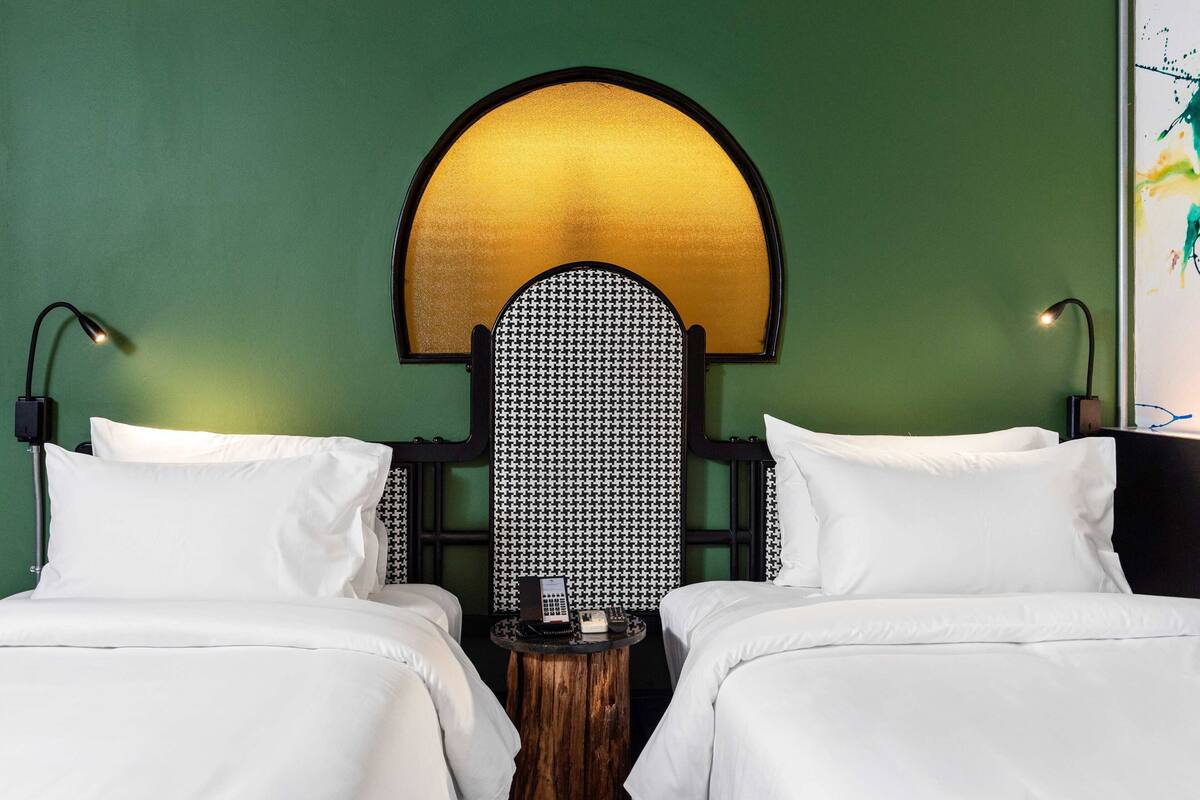 A hotel room with two beds, a round wooden side table, a telephone, and a wall-mounted light fixture.