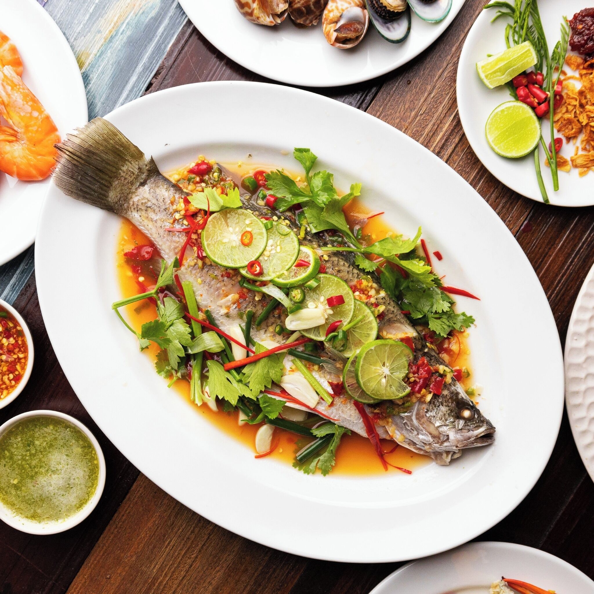 A plate of fish with lime and herbs, surrounded by other dishes and condiments.