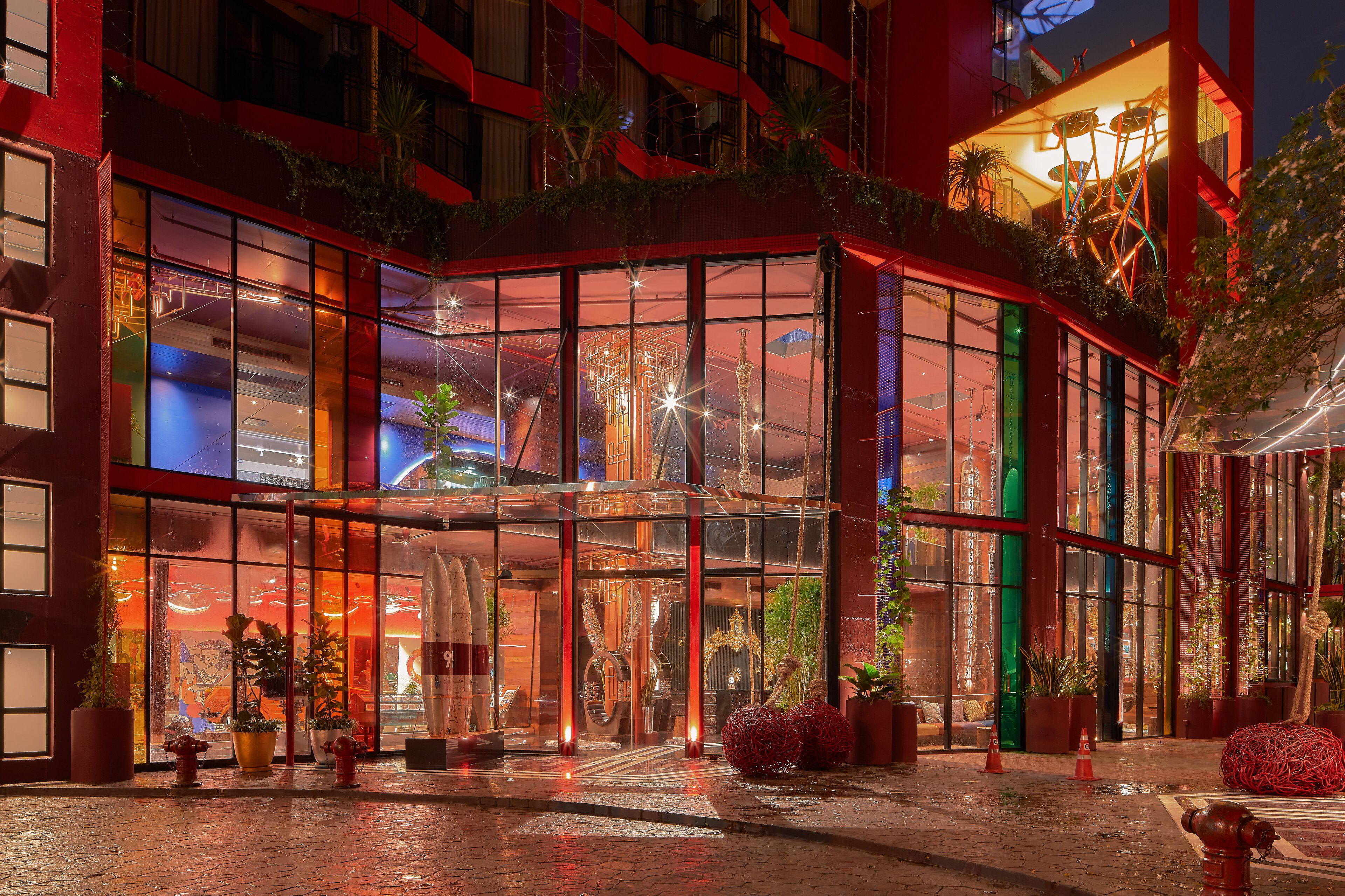 A modern hotel entrance with large glass doors, indoor plants, and a red exterior.
