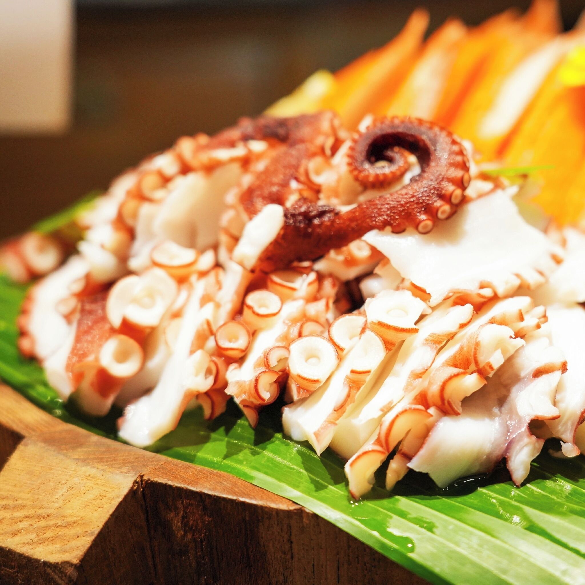 Una mesa de madera con tentáculos de pulpo y verduras cortadas sobre una hoja verde.