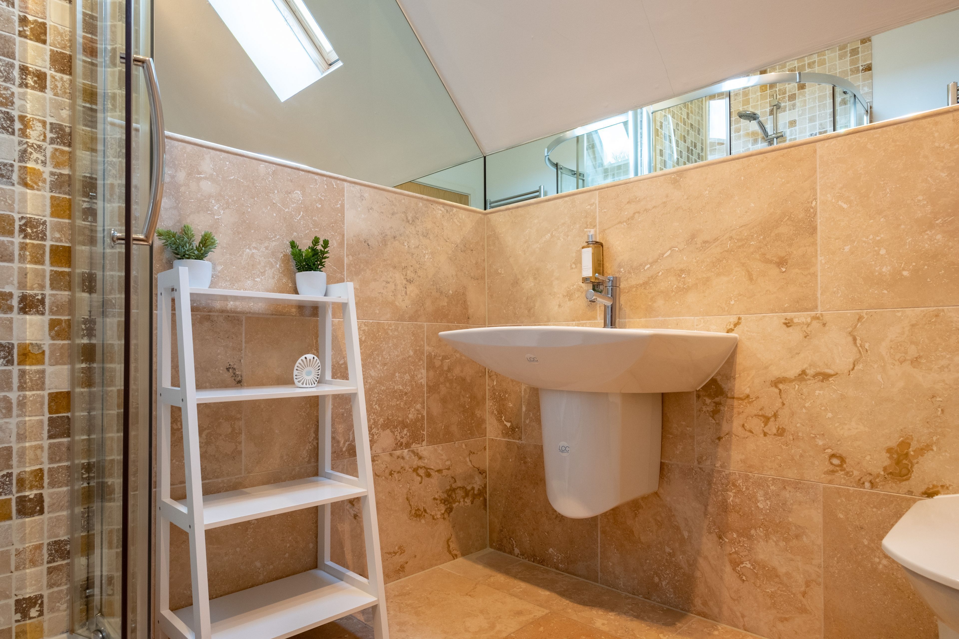 Une salle de bain avec une douche à parois de verre, un lavabo sur colonne blanc et un mur miroir.