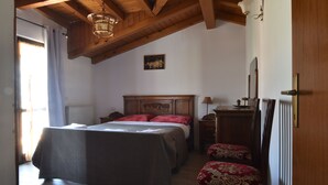 Une chambre avec un plafond en bois, un lit avec une literie rouge, une chaise avec un coussin rouge et une petite table avec une lampe.