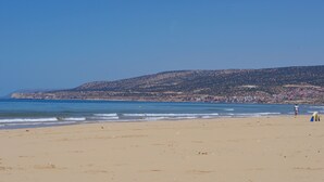 A beach with a clear sky, a sandy shore, and a hilly landscape in the background. - Azrac Surf Morocco (Aourir)