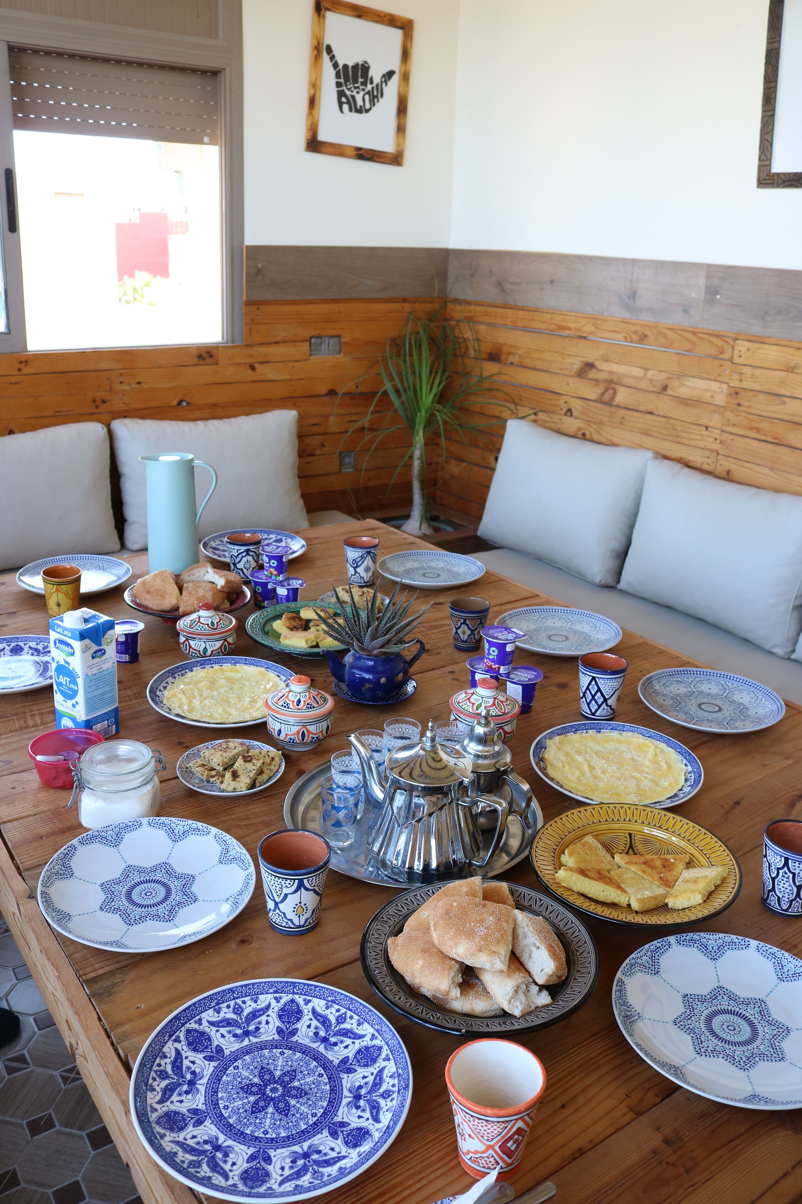 A dining table set with various plates, cups, and a pitcher, surrounded by wooden benches and cushions.