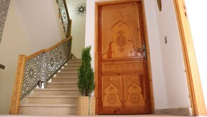 A wooden door with intricate carvings, a staircase with a decorative railing, and a small potted plant. - Azrac Surf Morocco (Aourir)