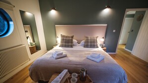 Ein ordentlich bezogenes Bett mit Kopfteil, ein Nachttisch mit Lampe sowie ein Tablett mit Buch, zwei Tassen und einer Kaffeekanne.