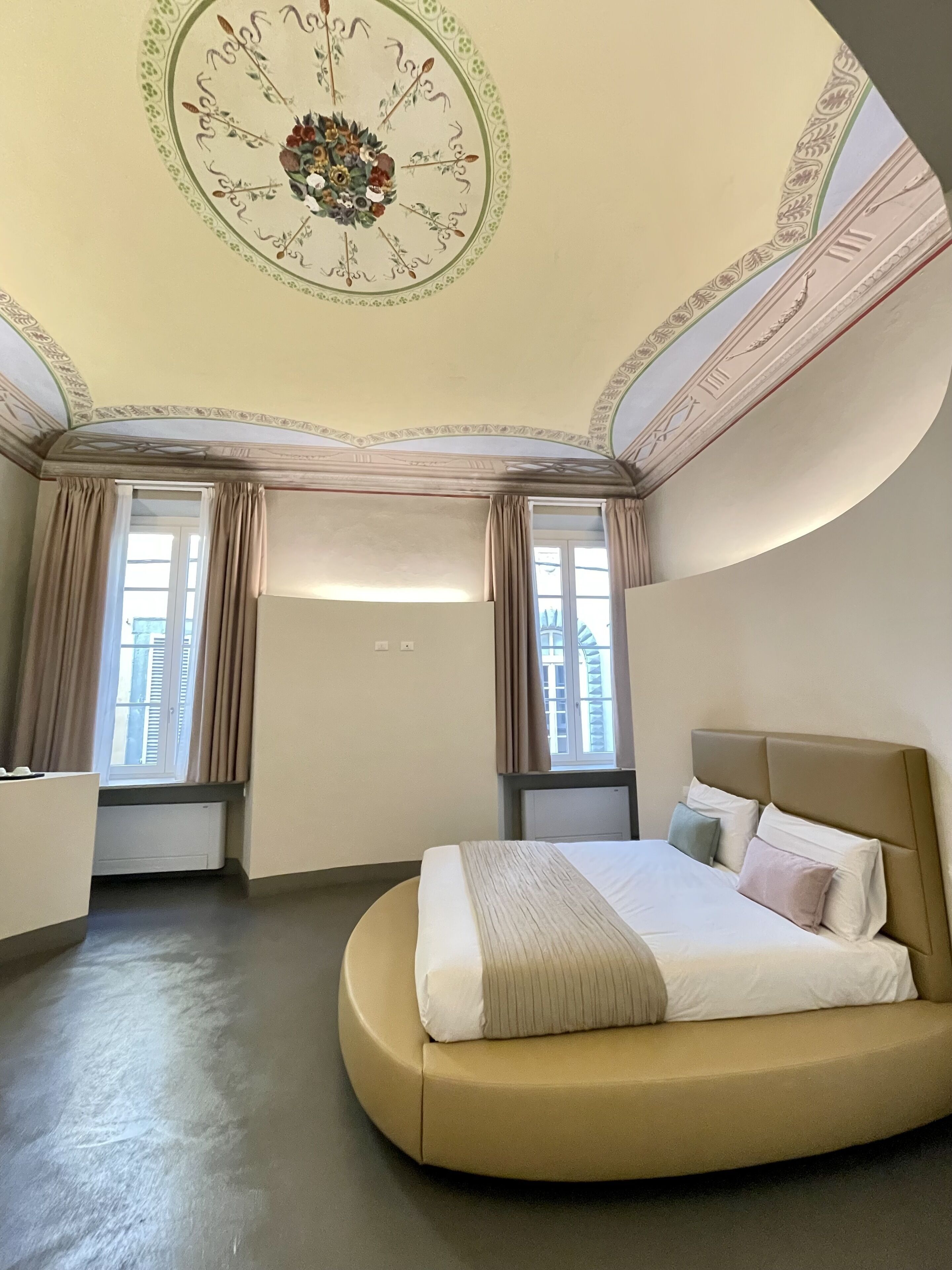 Un dormitorio con una cama curva, un techo decorativo y ventanas amplias con cortinas.
