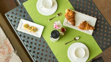 Una mesa con un mantel individual verde, dos platos blancos, un tarro de mermelada, una flor y un croissant.