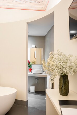Une salle de bain moderne avec une grande baignoire, un lavabo et un miroir. Un vase rempli de fleurs est posé sur le comptoir.