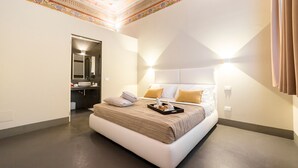 A modern hotel room with a large bed, a bathroom with a mirror, and a decorative ceiling. - LUCUS Exclusive B&B (Lucca)