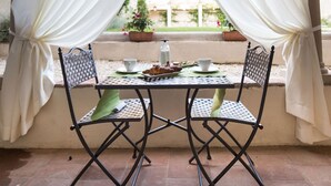 A covered outdoor seating area with two chairs and a table, featuring a view through a window with white curtains. - LUCUS Exclusive B&B (Lucca)