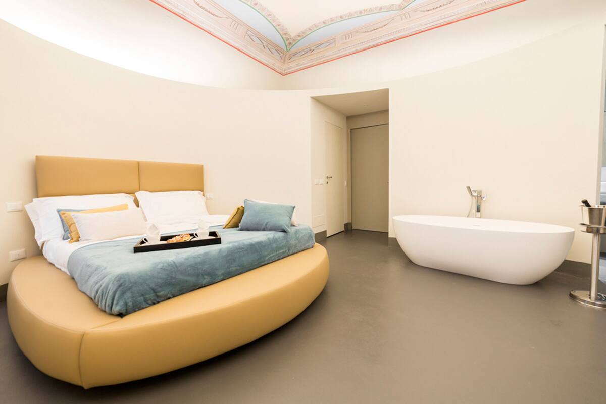 Un dormitorio moderno con una cama curvada, una bañera grande y un tragaluz.