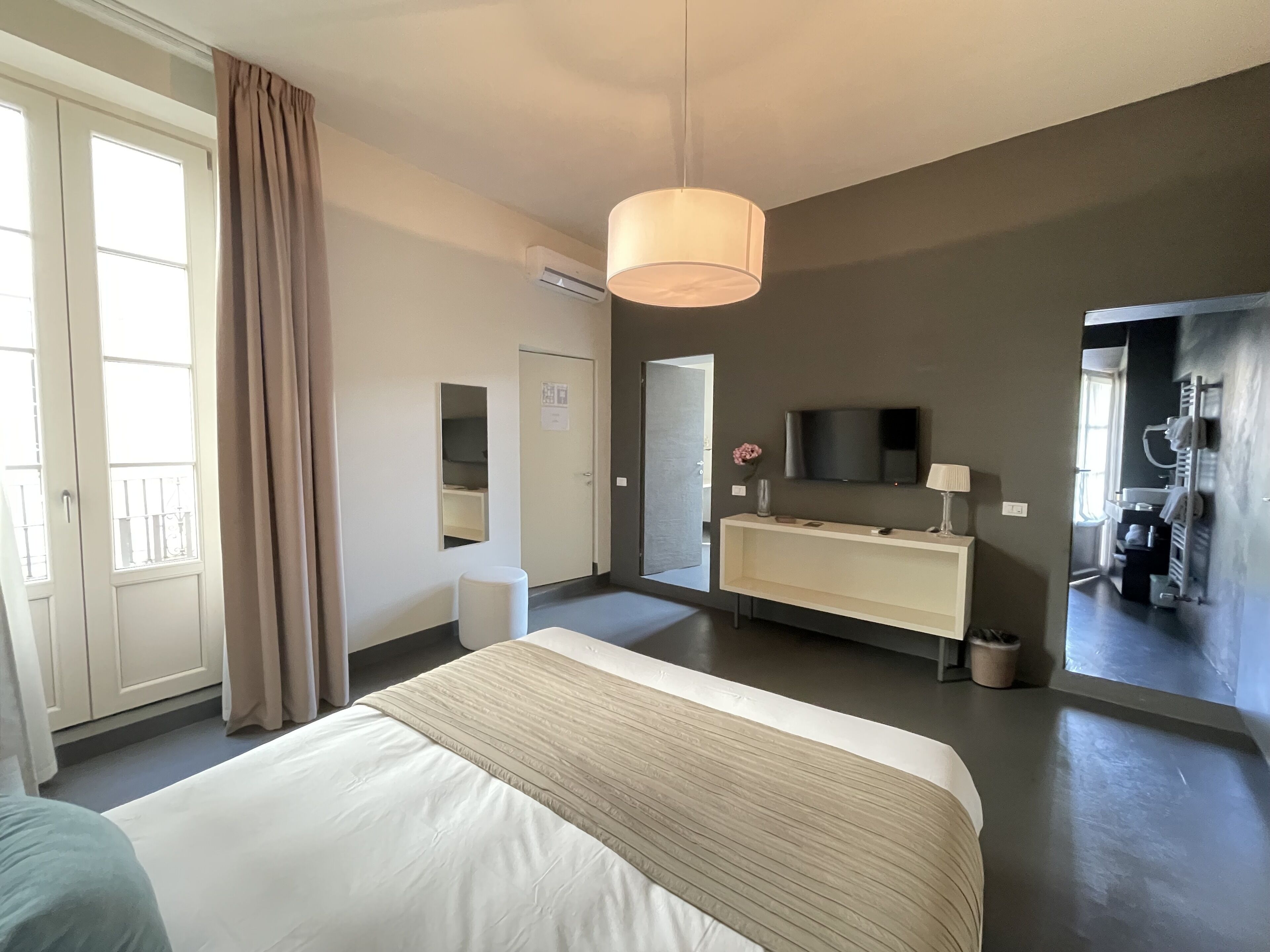 A modern hotel room with a large bed, a vanity with a mirror, a television, and a large window with curtains.