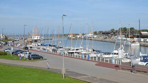 Ein Yachthafen mit zahlreichen Booten, die an der Uferpromenade liegen, einem Fußweg und einer Straße mit parkenden Autos.