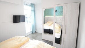 Ein modernes Schlafzimmer mit einem Bett, einem an der Wand montierten Fernseher und einem Schrank mit Spiegel.