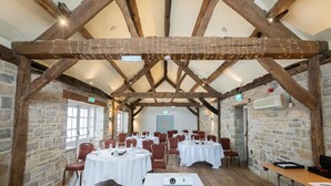 A conference room with wooden beams, stone walls, and round tables with chairs.