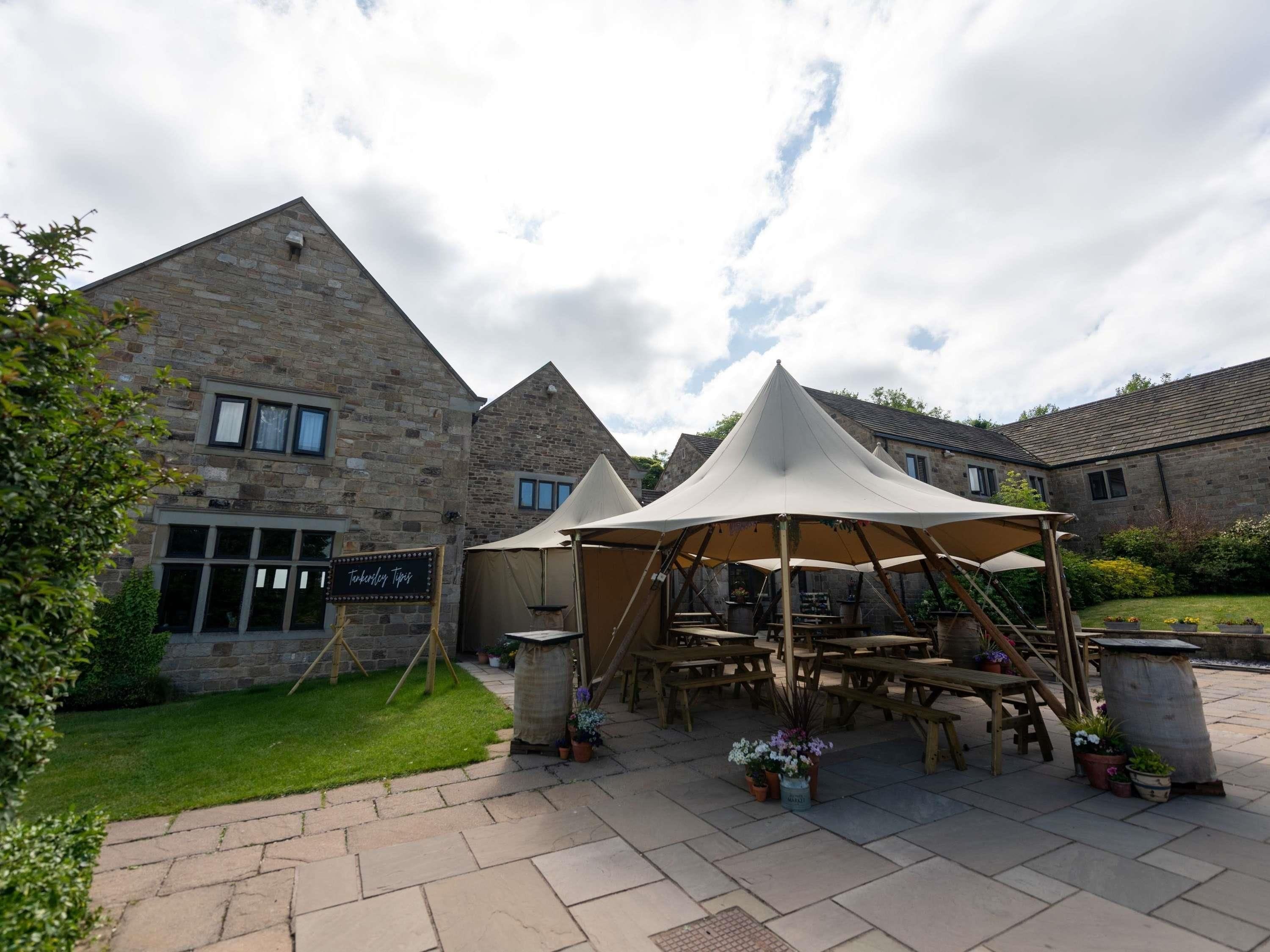 A courtyard with stone buildings, a tented area, and a signboard.
