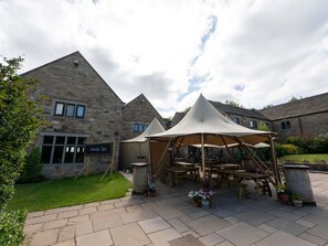 A courtyard with stone buildings, a tented area, and a signboard.