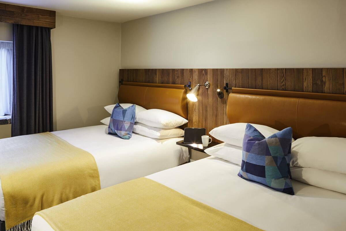 Habitación de hotel con dos camas, cabeceros de madera, lámparas de noche y una ventana con cortinas.