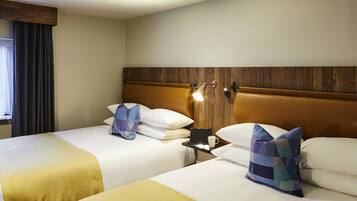 A hotel room with two beds, wooden headboards, bedside lamps, and a window with curtains.