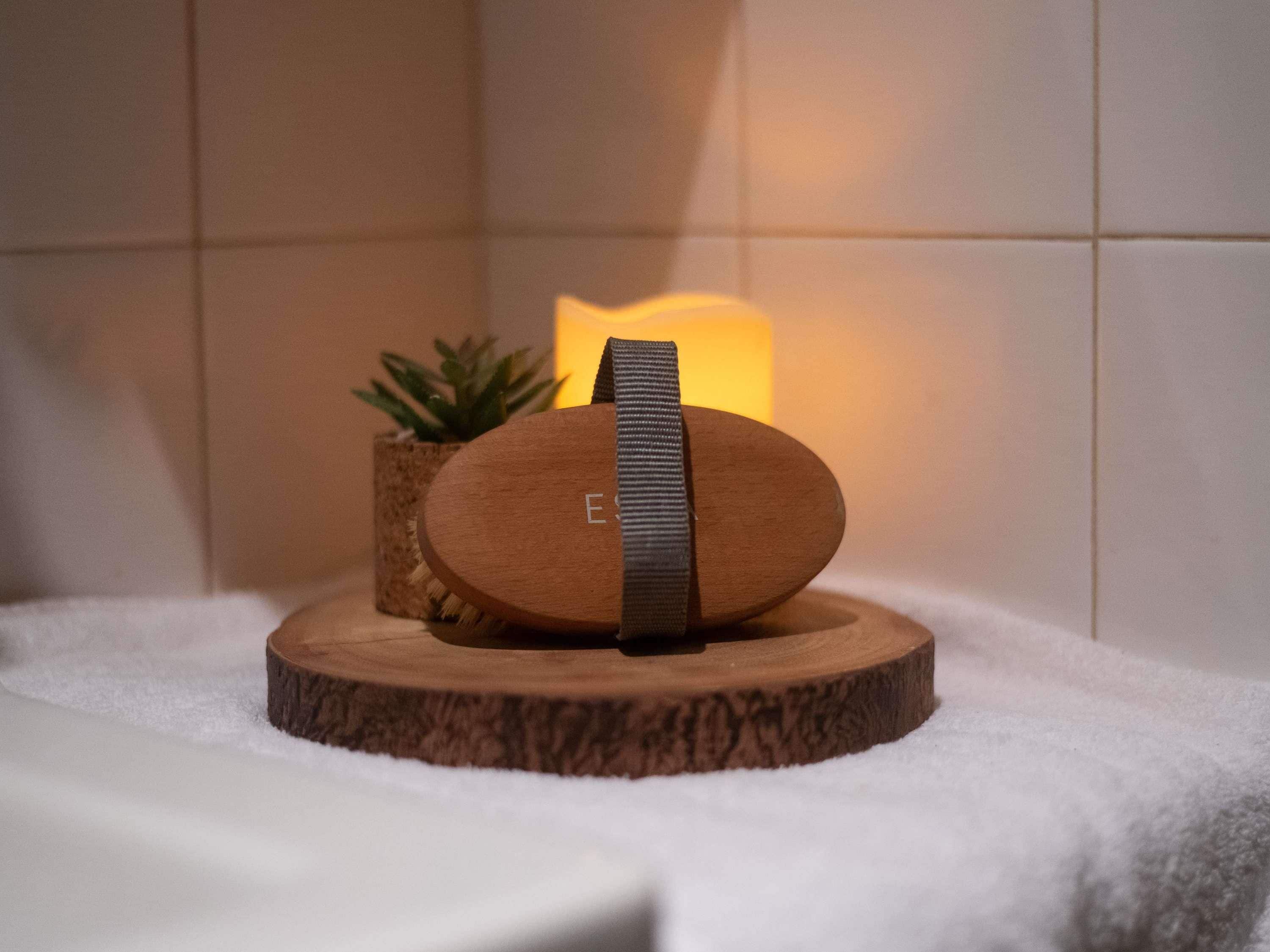 A wooden object with a strap on a round wooden base, a lit candle, and a small plant in the background.