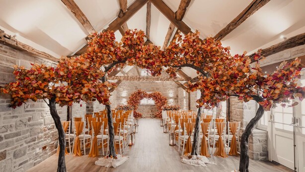 An indoor venue with a stone wall, wooden beams, and a central aisle with chairs.