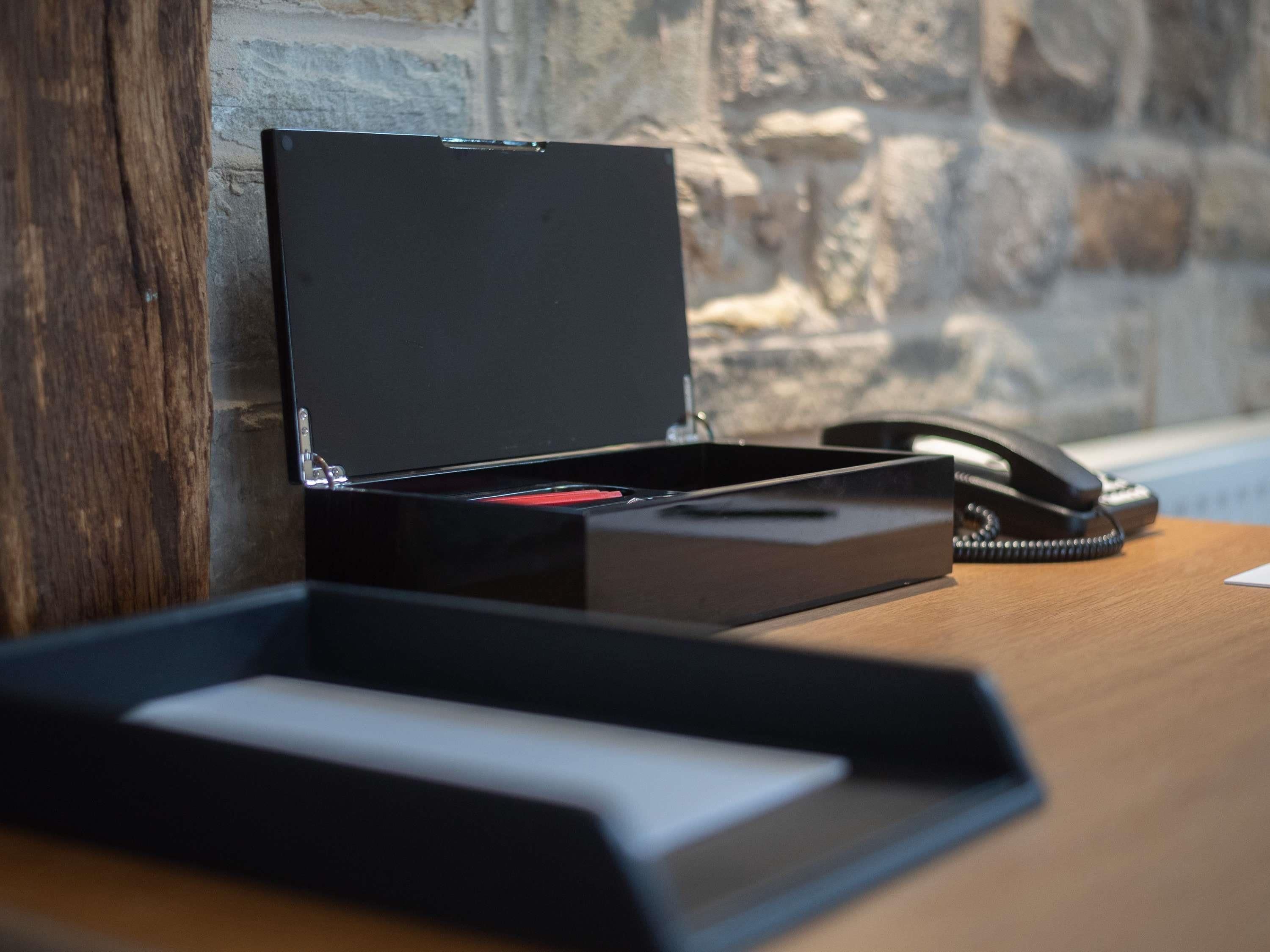 A desk with a closed black box, a telephone, and a wooden surface.