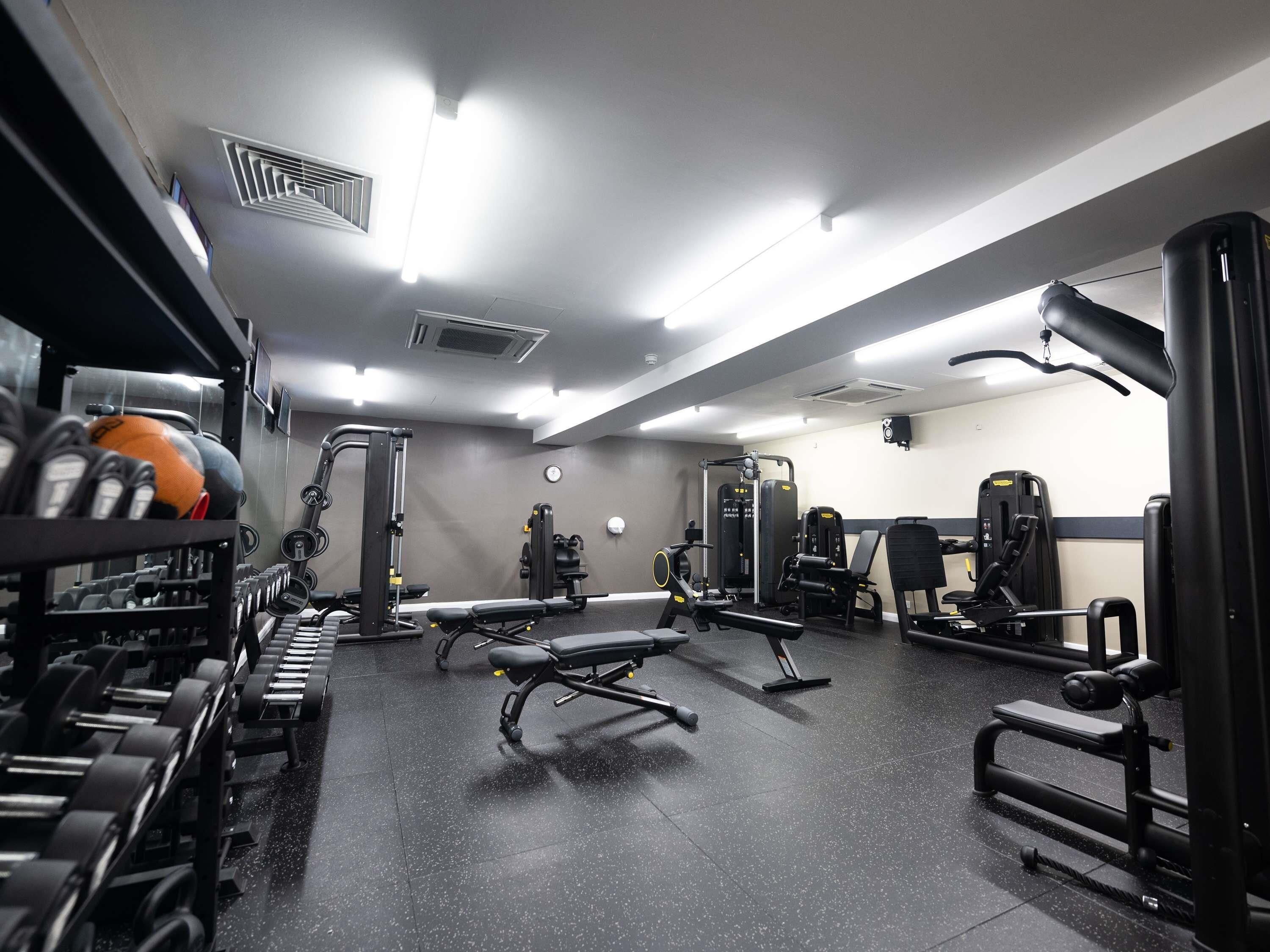 Un gimnasio con diversos equipos de ejercicio, como mancuernas, bancos y máquinas de pesas.