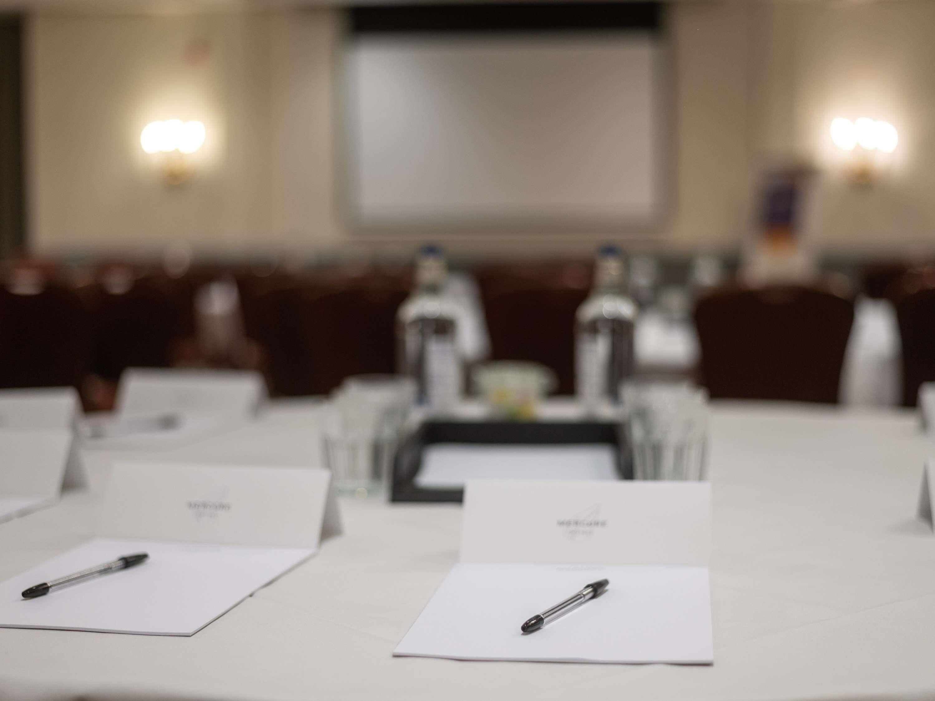 Une salle de conférence équipée de tables, de chaises, de plaques nominatives et de stylos posés sur les tables.
