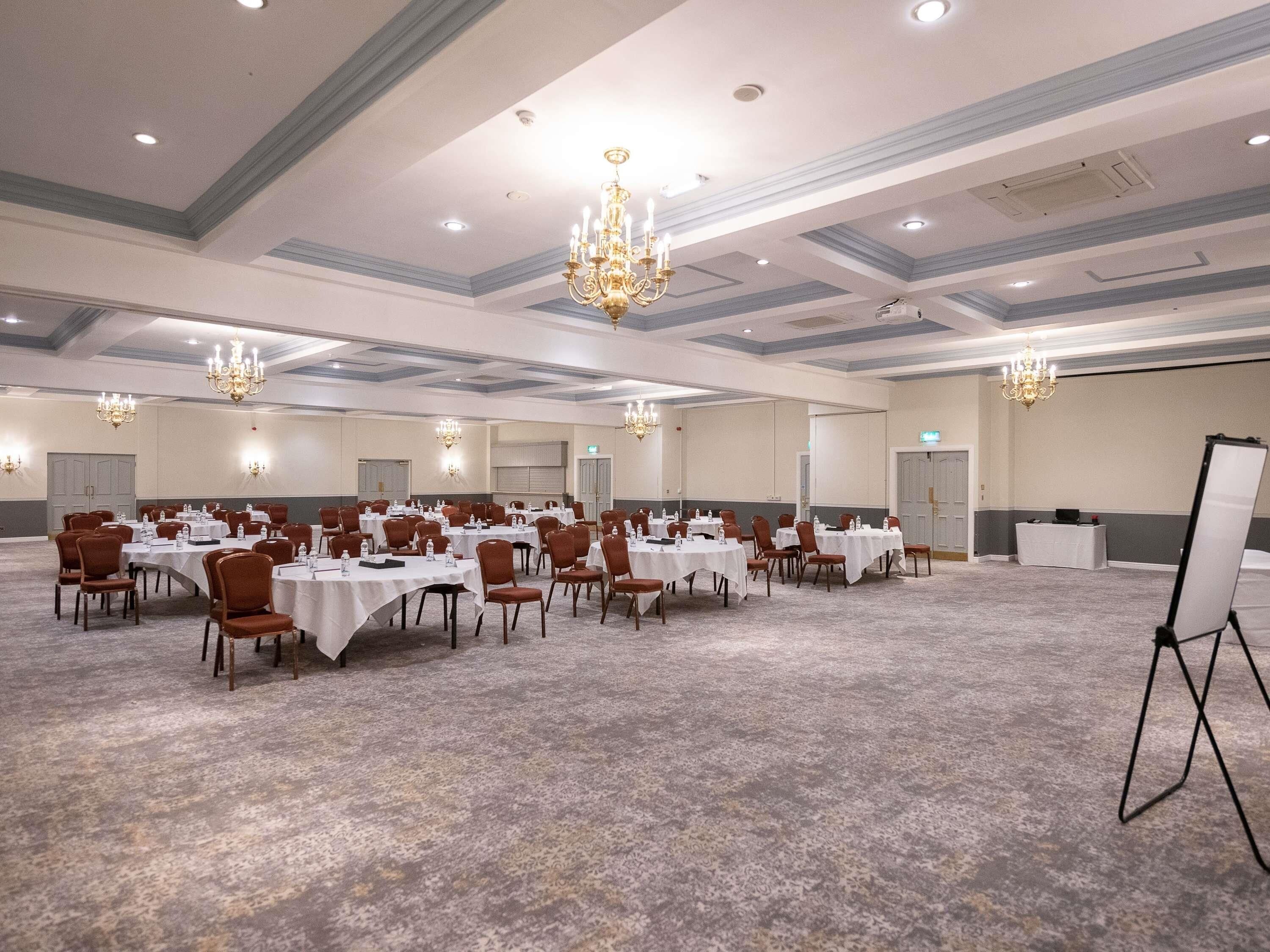 Un amplio salón de conferencias con mesas y sillas, candelabros y una pizarra.