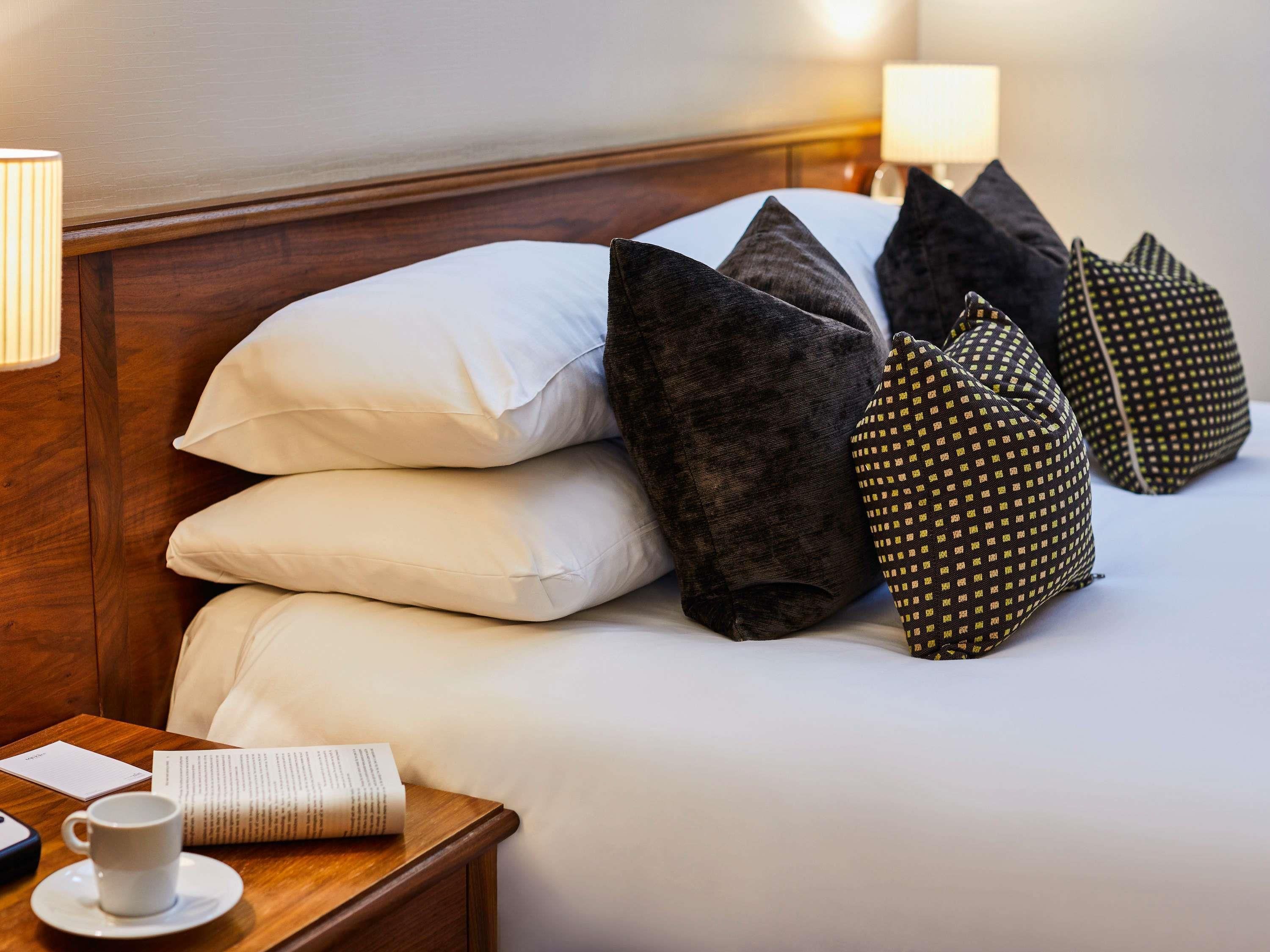 A neatly made bed with pillows, a bedside table with a cup and a menu, and a lamp.