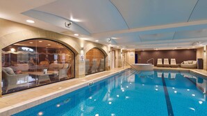 An indoor swimming pool with a glass wall, lounge chairs, and a no diving sign.