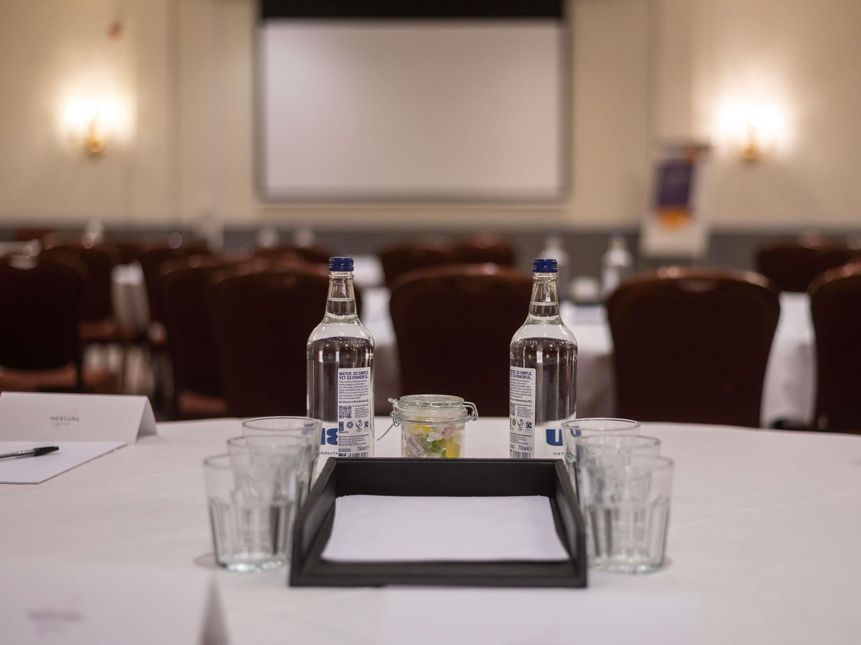 A conference room with two bottles of water, a glass jar, and a black tray on a table.