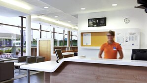 Un moderno mostrador de recepción con una pantalla digital, un reloj y carteles informativos.