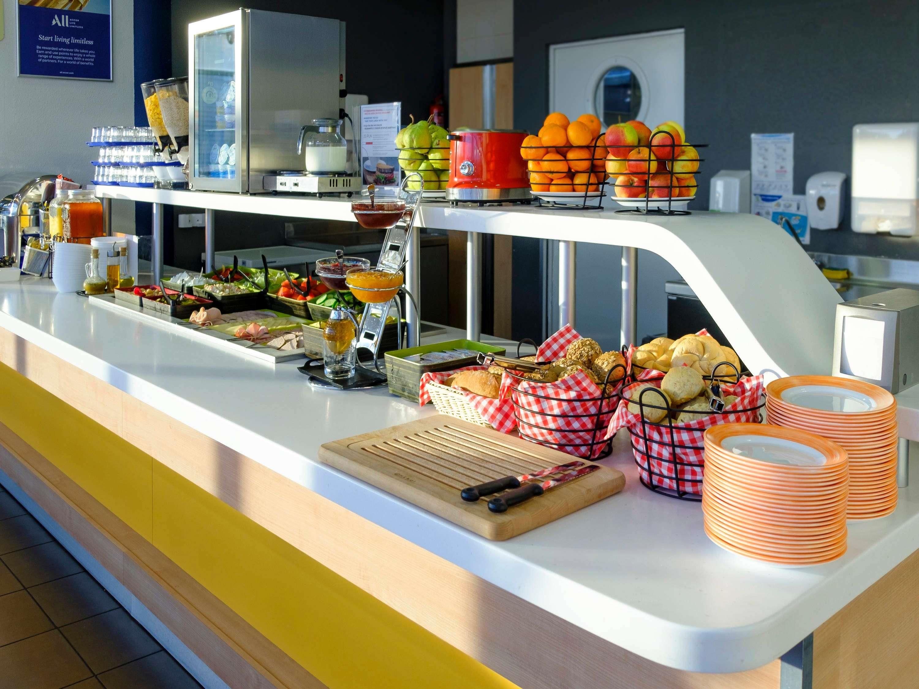A buffet counter with various food items, a coffee machine, and a fruit display.