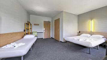 Habitación de hotel con dos camas individuales, cabecero de madera, una silla verde, armario de madera y una lámpara fijada a la pared.