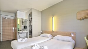 Una habitación de hotel con dos camas, un baño y un espejo.