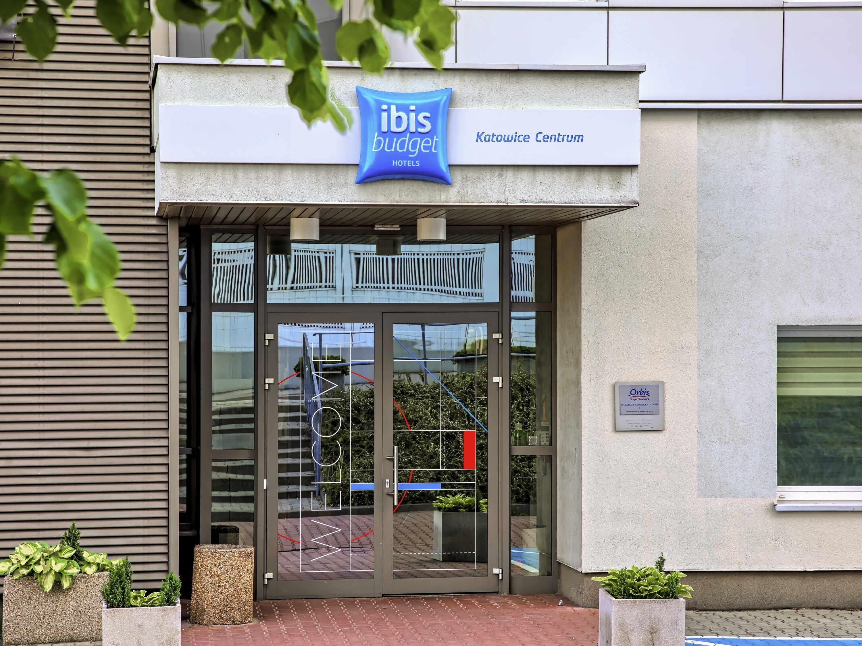 Ein Hotel Eingang mit Glastür, einem Schild für 'Ibis Budget Katowice Centrum' und einem 'Willkommen'-Schild an der Tür.