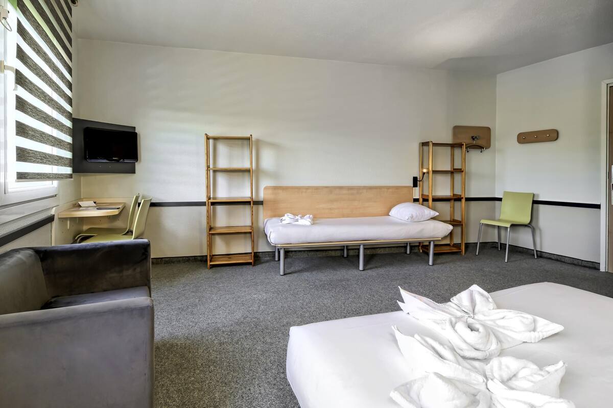 A hotel room with a bed, a desk, a chair, a TV, and a window with blinds.