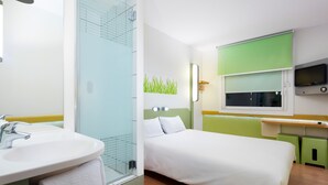 Una habitación de hotel con baño, una cama, un televisor y una pared verde.