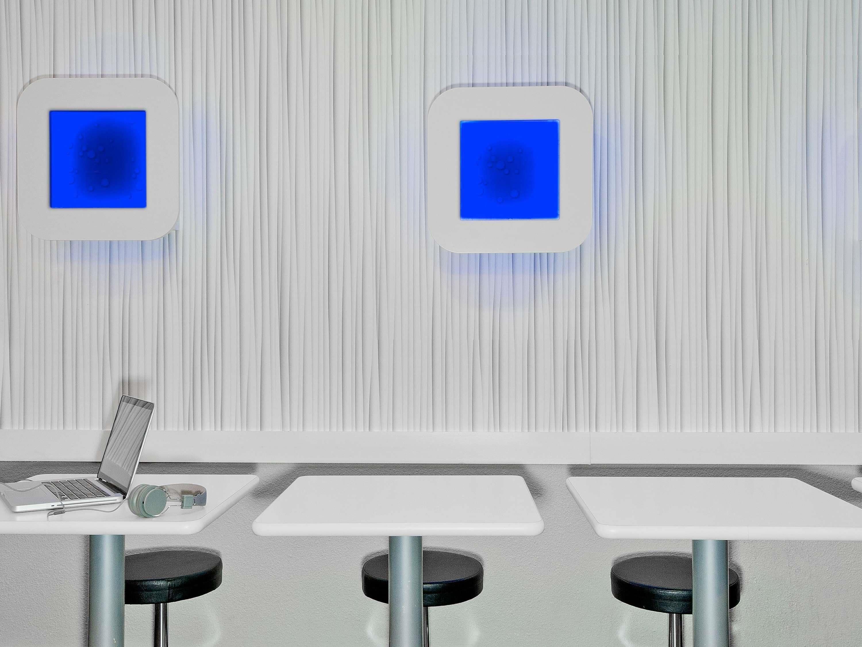 A modern, minimalist room with two white tables, one with a laptop and headphones, and two stools.