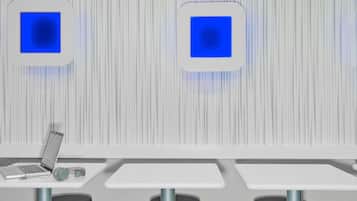 Una habitación moderna y minimalista con dos mesas blancas, una con una computadora portátil y auriculares, y dos taburetes.