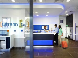 A reception desk with a blue accent, a sign reading 'WITAMY CIE,' and a computer monitor. - ibis budget Warszawa West Station (Warsaw)