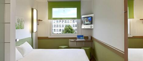 Habitación de hotel con cama, escritorio, laptop, televisor y ventana con vista a edificios.