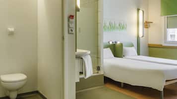 Una camera d'albergo con il water, una doccia, un letto e una lampada fissata al muro.