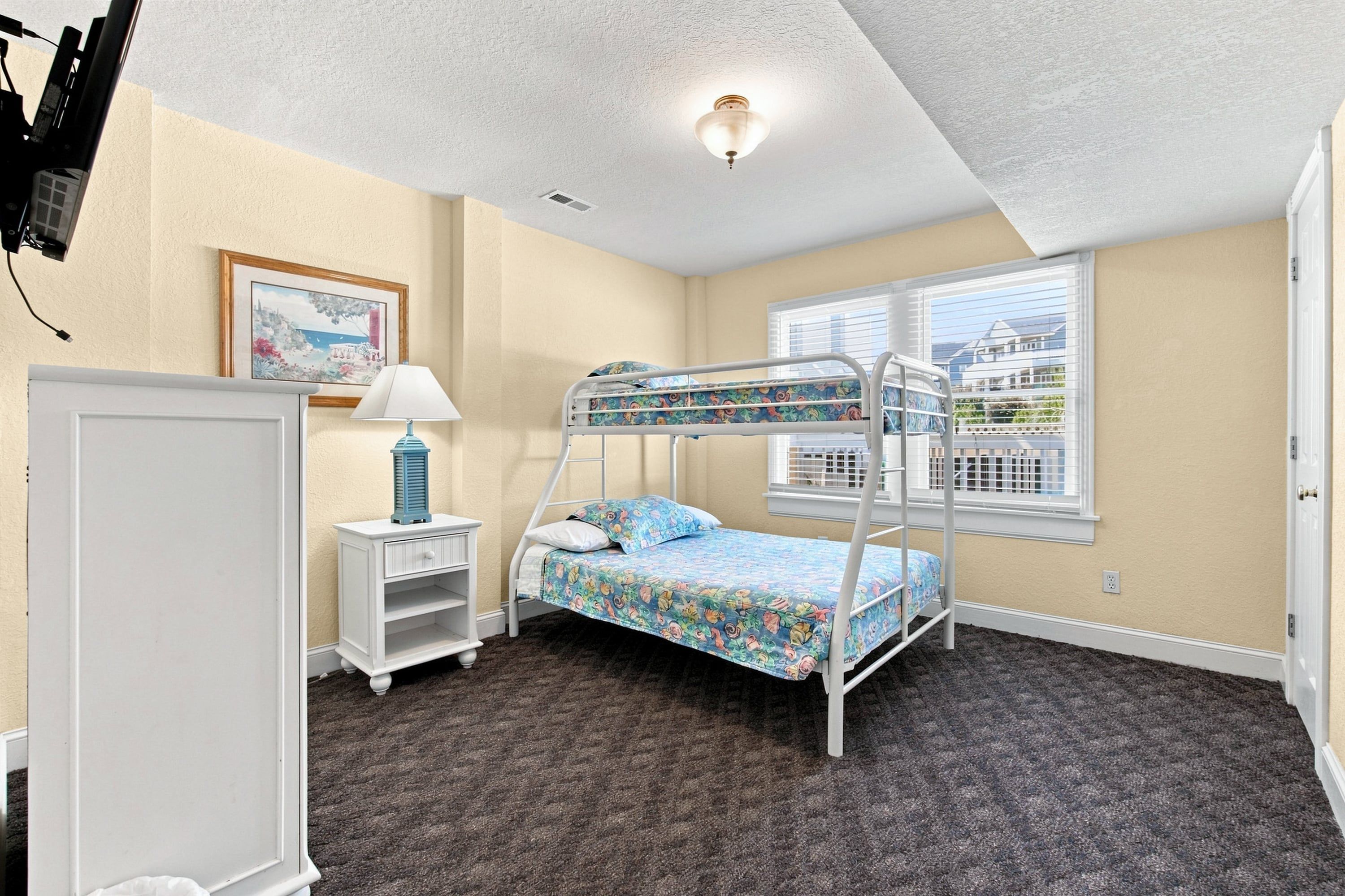 A bunk bed room with a window, a desk, and a lamp.
