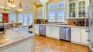 A spacious kitchen with white cabinetry, a large island, and a view of the city through the windows. - AMAZING HOME in Four Seasons in Duck! Private Pool! 10% OFF available summer weeks! (Duck)