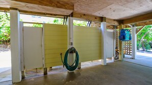 A covered outdoor area with a concrete floor, a yellow door, and a green hose coiled on the floor. - AMAZING HOME in Four Seasons in Duck! Private Pool! 10% OFF available summer weeks! (Duck)